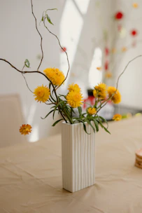 A close-up of a textured stoneware vase in cheerful yellow, holding fresh wildflowers.