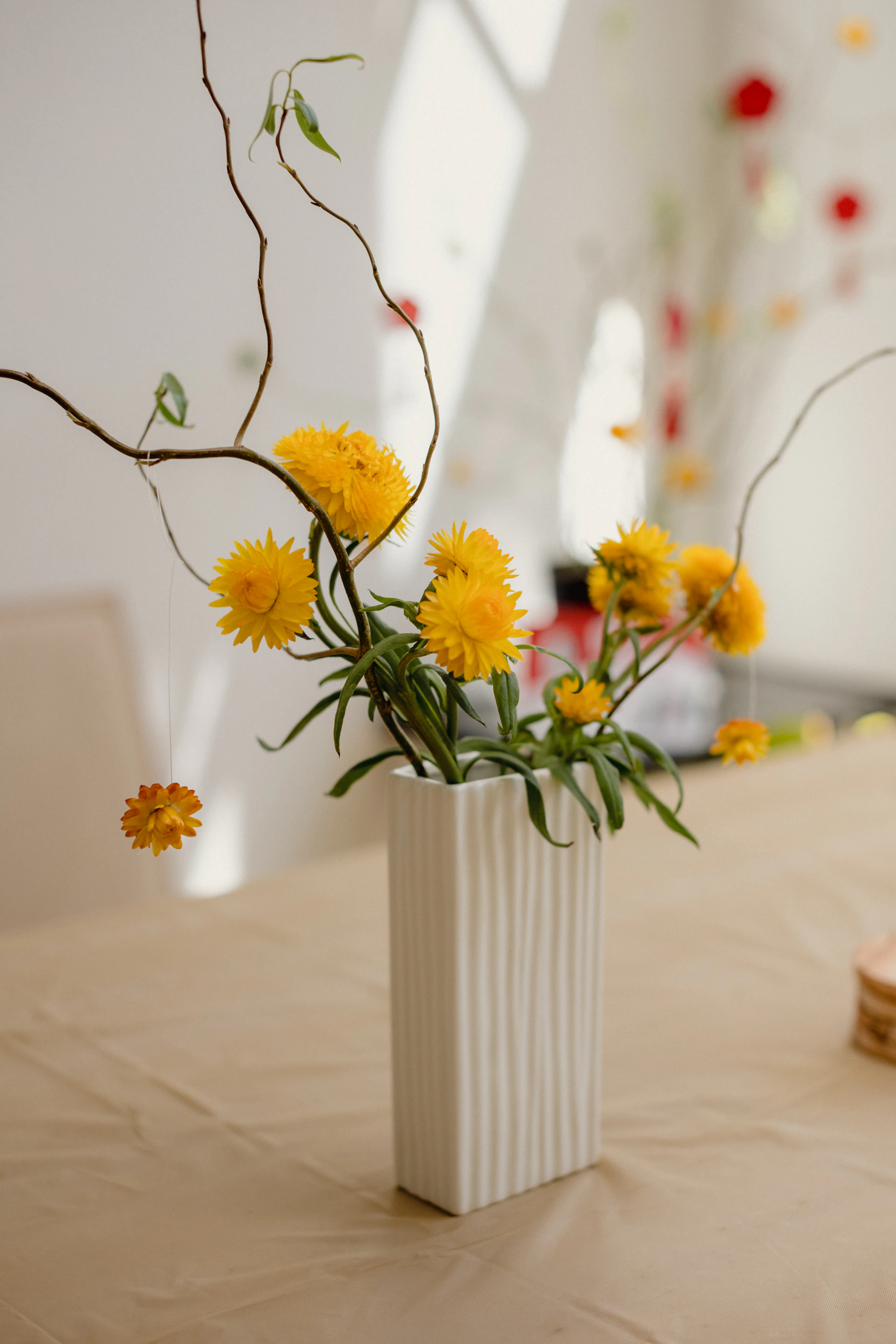 a white vase filled with yellow flowers on top of a table