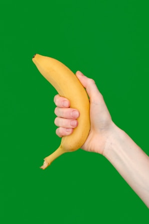 a hand holding a banana on a green background