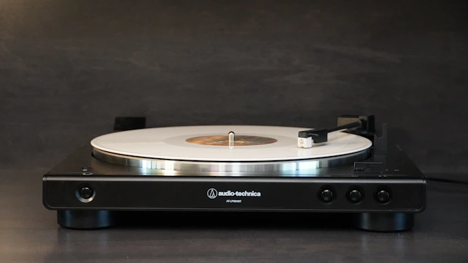 A sleek black and white photo of a modern turntable with a vinyl record spinning, set against a minimalist background.