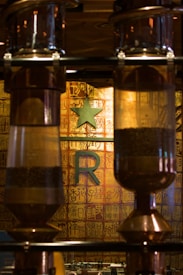 Large, glass coffee bean chambers are set against a backdrop featuring intricate, gold and ochre patterns with Chinese characters. A prominent green star and a large letter R are mounted on the wall, hinting at a themed interior related to coffee or a specific brand.