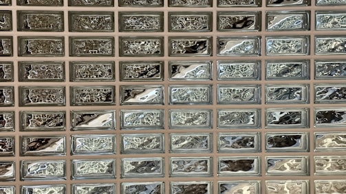A grid of rectangular glass blocks with a reflective, wavy pattern on their surfaces, arranged in a uniform, tiled fashion.