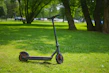 A sleek electric scooter parked on a sunny urban street with greenery in the background.