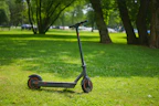 A sleek electric scooter parked on a sunny urban street with greenery in the background.