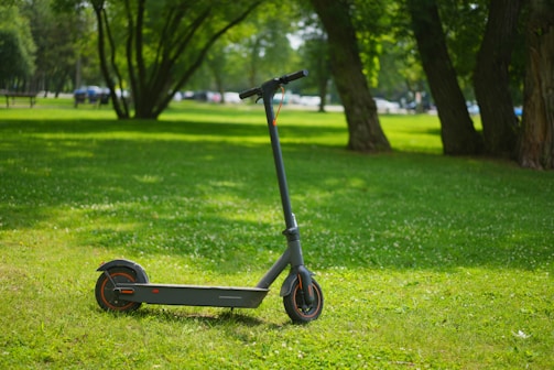 A sleek black electric scooter parked on a city street with green trees in the background.