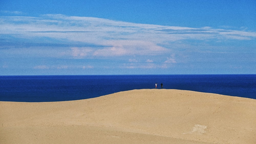 a couple of people standing on top of a sandy hill