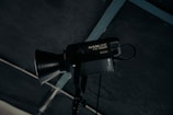 A professional studio light fixture with the label 'NANLITE FS-300B' is mounted and positioned against a dark ceiling with a grid structure. The light has a large conical reflector and appears to be turned off.