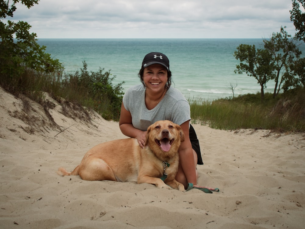 a woman kneeling down next to a dog on a beach