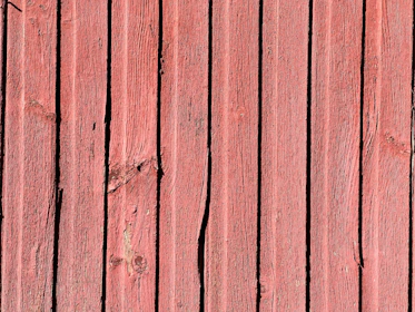 Vertical wooden planks with a reddish hue, displaying natural textures and grain patterns. Some planks have visible knots and imperfections, adding to the rustic appearance.