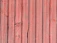 Vertical wooden planks with a reddish hue, displaying natural textures and grain patterns. Some planks have visible knots and imperfections, adding to the rustic appearance.