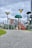 A modern playground featuring various climbing structures, slide, and benches is set under a cloudy sky. The playground includes green, tree-like structures and metal frameworks, with a visible slide and other play equipment. The scene is surrounded by grass and a paved walkway.