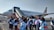 A group of people, many of whom appear to be students with backpacks, are boarding a commercial airplane on an airport tarmac. The airplane is branded with 'SUPER AIR JET' and features a jet bridge or mobile stairs for entry.