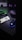 A dark, dimly lit workspace featuring a mechanical keyboard with green backlighting, a smartphone displaying a phone number, a backlit gaming mouse, and a set of headphones. The atmosphere appears to be that of a gaming or tech setup.