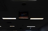 A dimly lit indoor ceiling with several fluorescent light panels. In the center, there is a backlit sign that reads 'KENO THIS WAY' with a partially visible arrow pointing directionally.