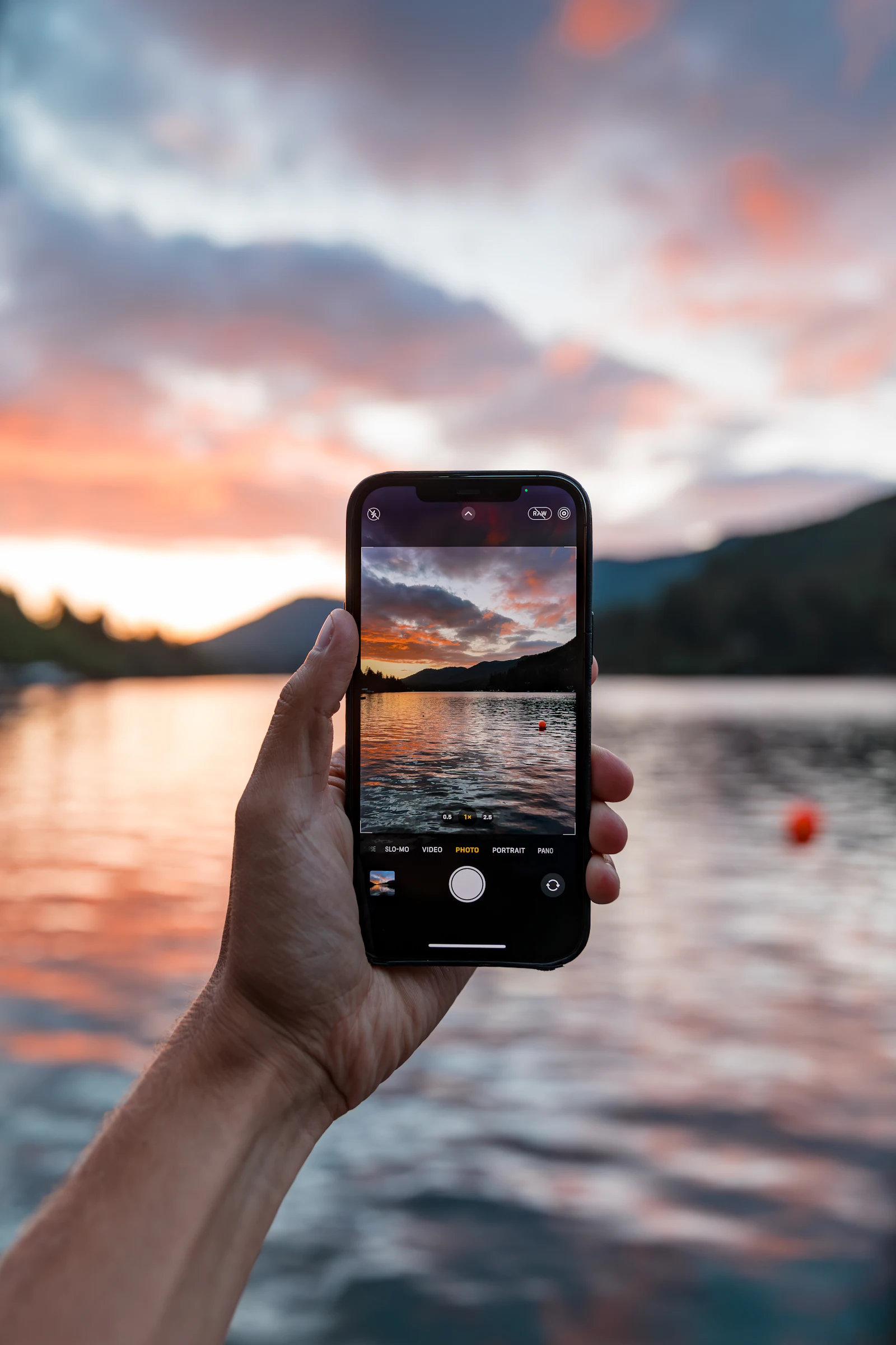Hand holding up a smartphone against an orange sunset over a lake to check it is eSIM compatible before a trip