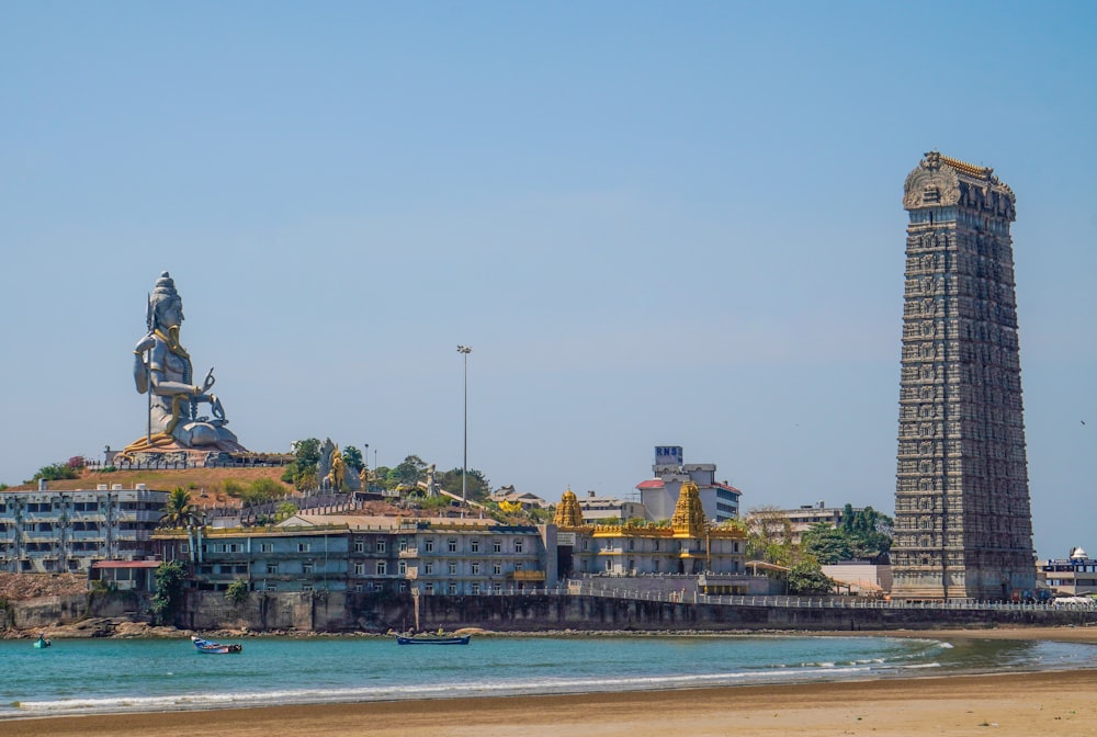 ein hoher Turm mit einer Statue darauf neben einem Gewässer