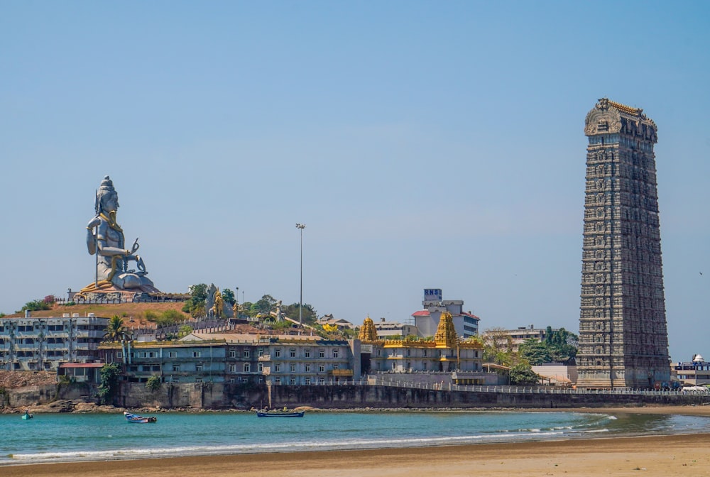 una torre alta con una estatua en la parte superior junto a un cuerpo de agua