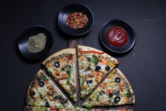 A person slicing a colorful vegetable pizza on a wooden board.