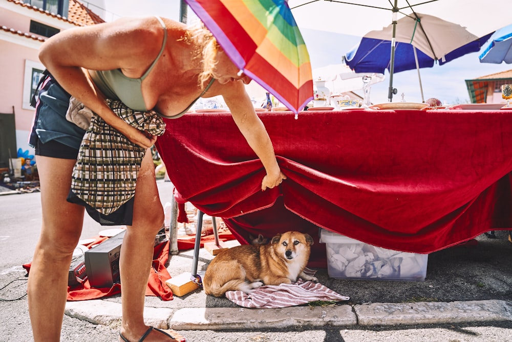 a woman bending over a table with a dog under it