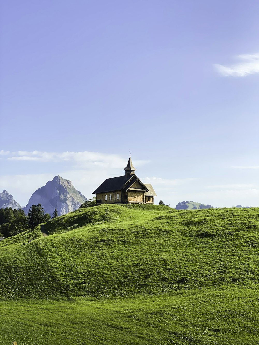 a church on a grassy hill with mountains in the background