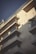 A modern apartment building featuring multiple balconies. The structure is bathed in soft, late-afternoon light, creating distinct shadows against the ivory facade. A potted palm is visible on one of the balconies, adding a tropical touch.
