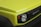 A close-up view of a yellow-green vehicle's front section, focusing on the sleek hood and the right headlight with a visible name badge on the grille. The design features a modern, bold aesthetic with smooth contours.