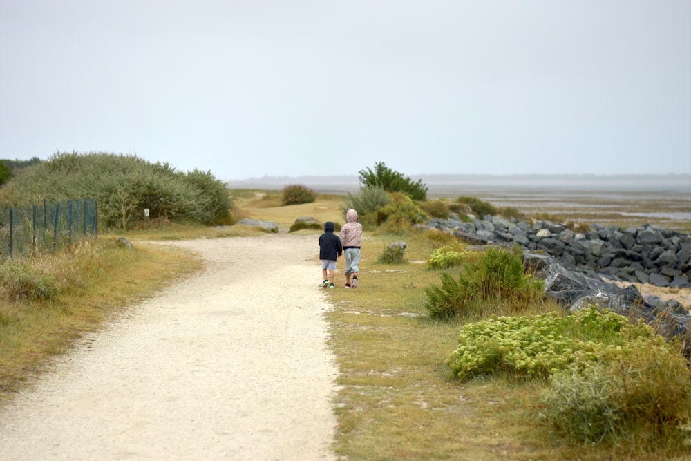 a couple of people walking down a dirt road