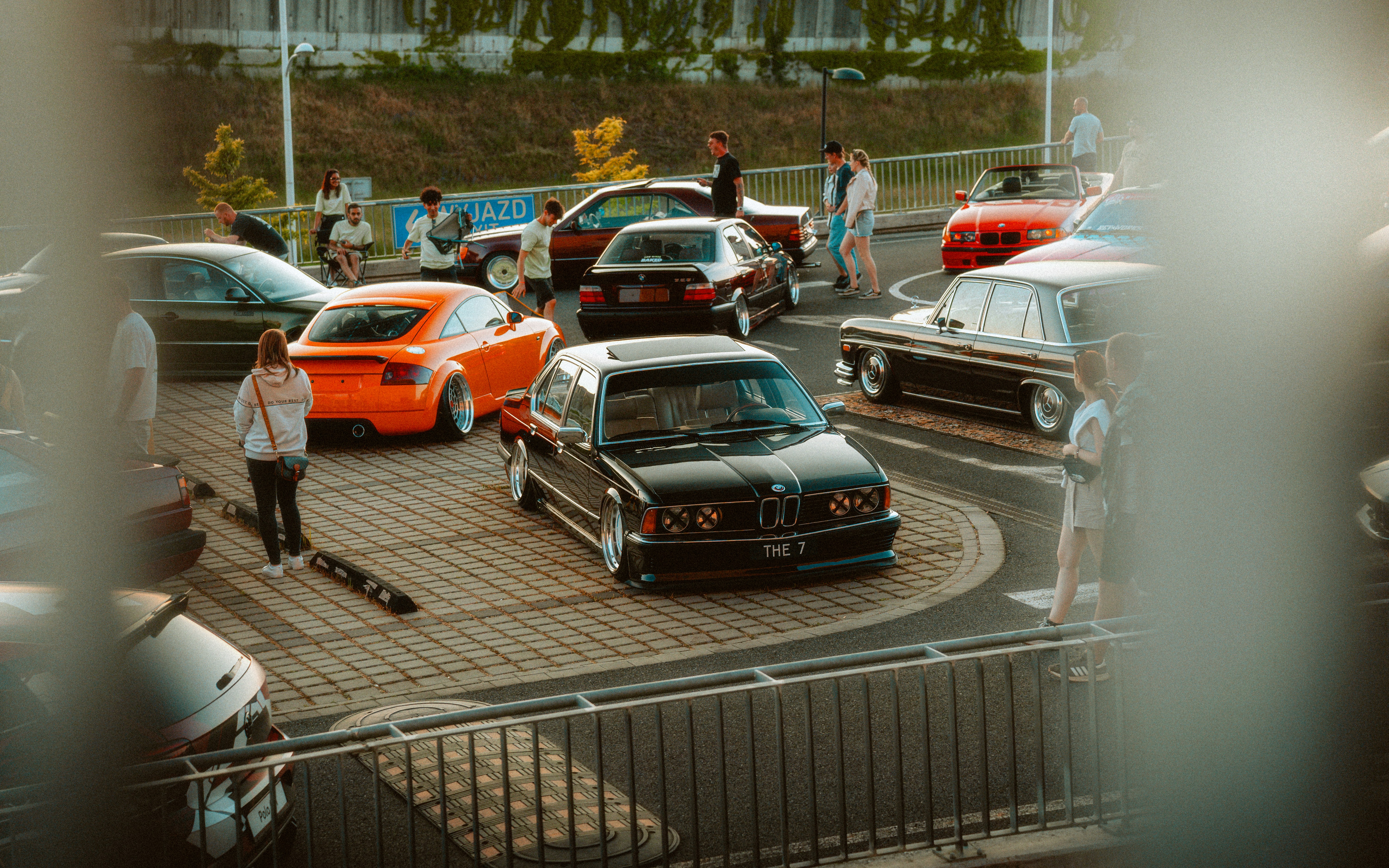 People gather to look at customized cars in a parking lot.