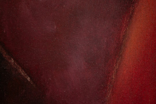 A textured surface with dark and rich maroon and burgundy hues blending seamlessly with hints of black and rust colors. The composition appears abstract and painterly, exhibiting depth and warmth through its color palette.