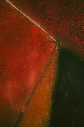 An abstract composition featuring intersecting geometric shapes with textured surfaces in rich, earthy tones. The sharp triangular form cuts across with gradients of red transitioning into dark green and orange.