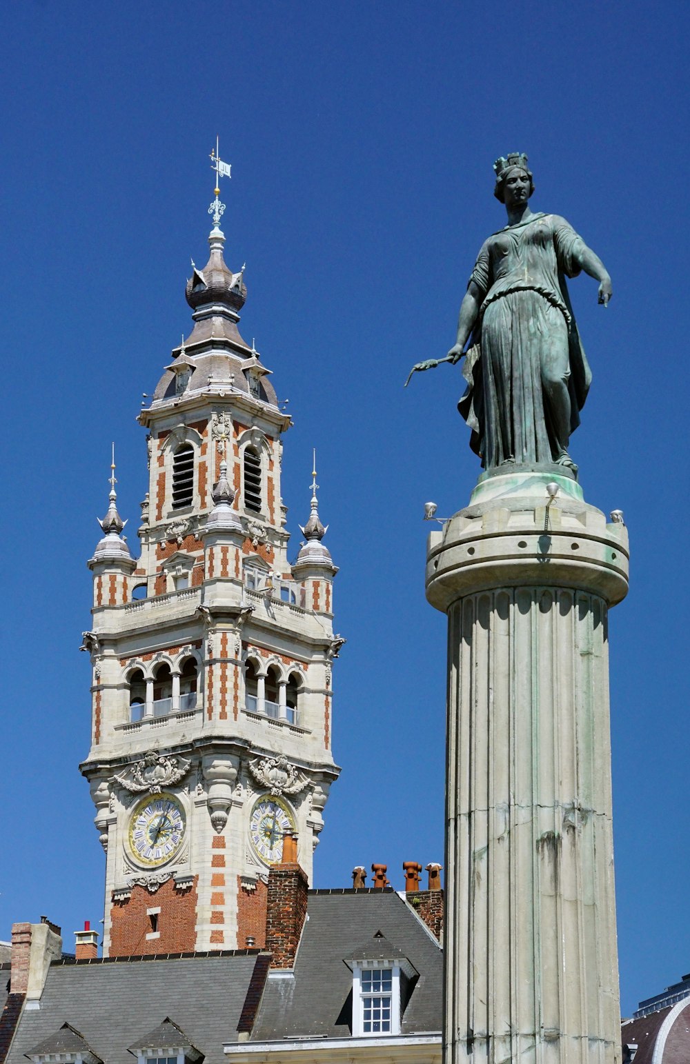 un grand bâtiment avec une tour de l’horloge à côté d’une statue