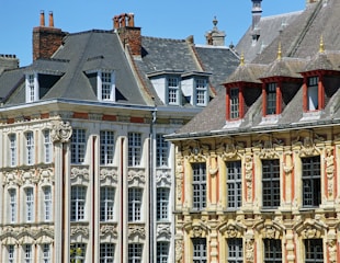 Elegant historic buildings featuring ornate architectural details, large windows, and steep slate roofs. The facades are richly decorated with sculptural elements and detailed moldings, reflecting classical European design.