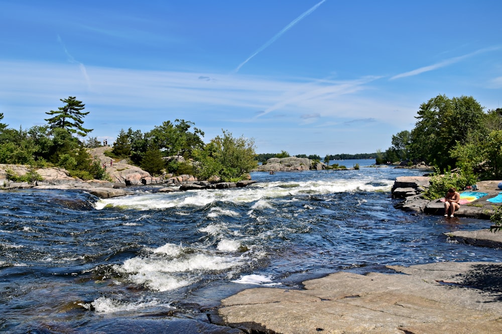 a person sitting on a rock next to a river