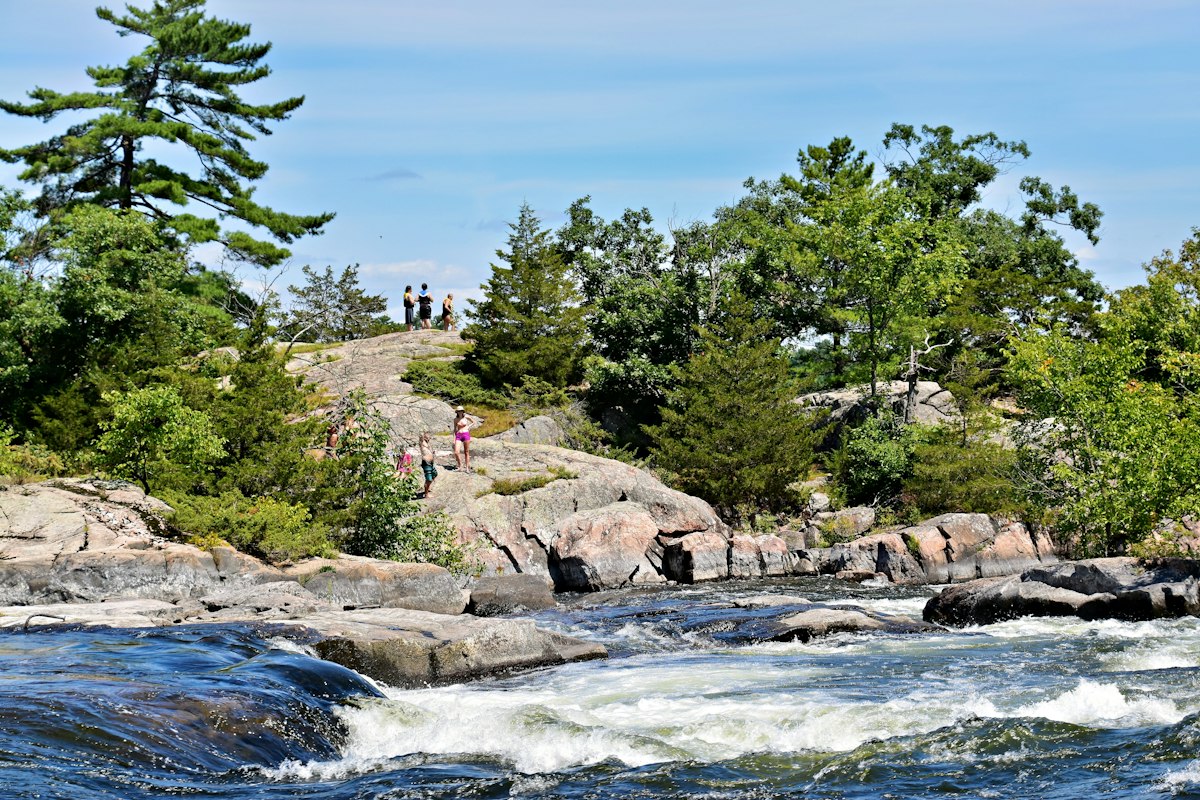 People exploring rocks beside a river in a green valley