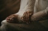 Close-up of hands entwined, with the bride’s delicate jewelry catching the soft glow of terra-cotta pink walls.