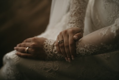 Close-up of hands entwined, with the bride’s delicate jewelry catching the soft glow of terra-cotta pink walls.