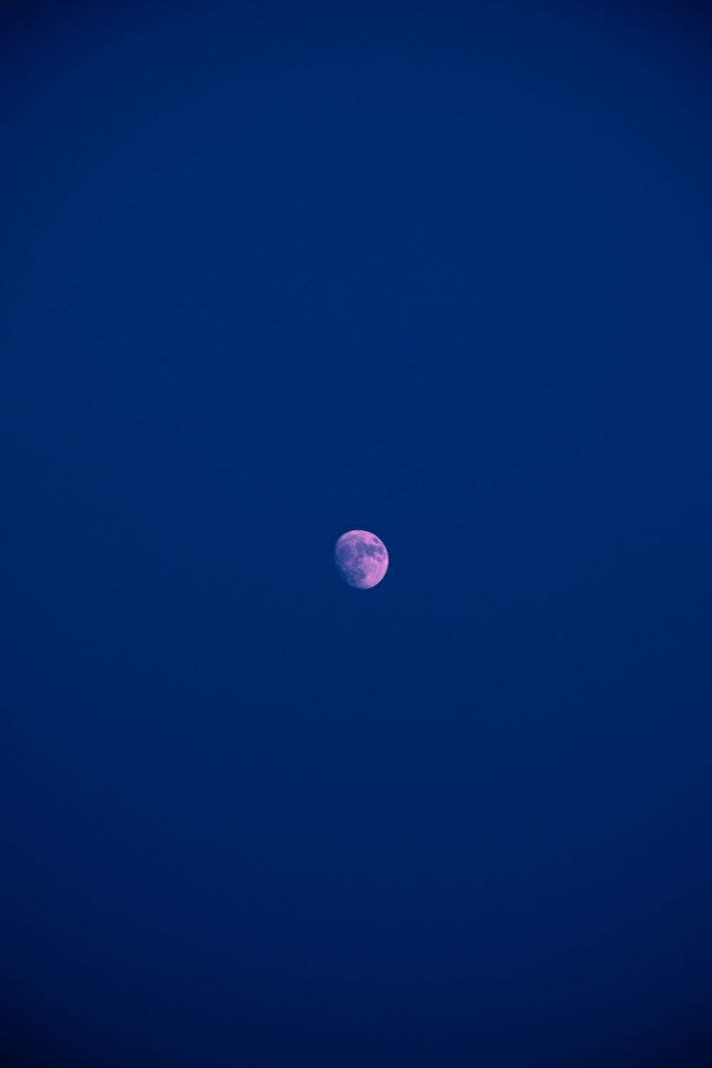 a full moon is seen in the blue sky