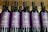 Several bottles of red wine are displayed in a row. The labels on the bottles are purple with gold lettering, indicating they are part of The Hess Collection, specifically the Allomi Napa Valley Cabernet Sauvignon from 2019.