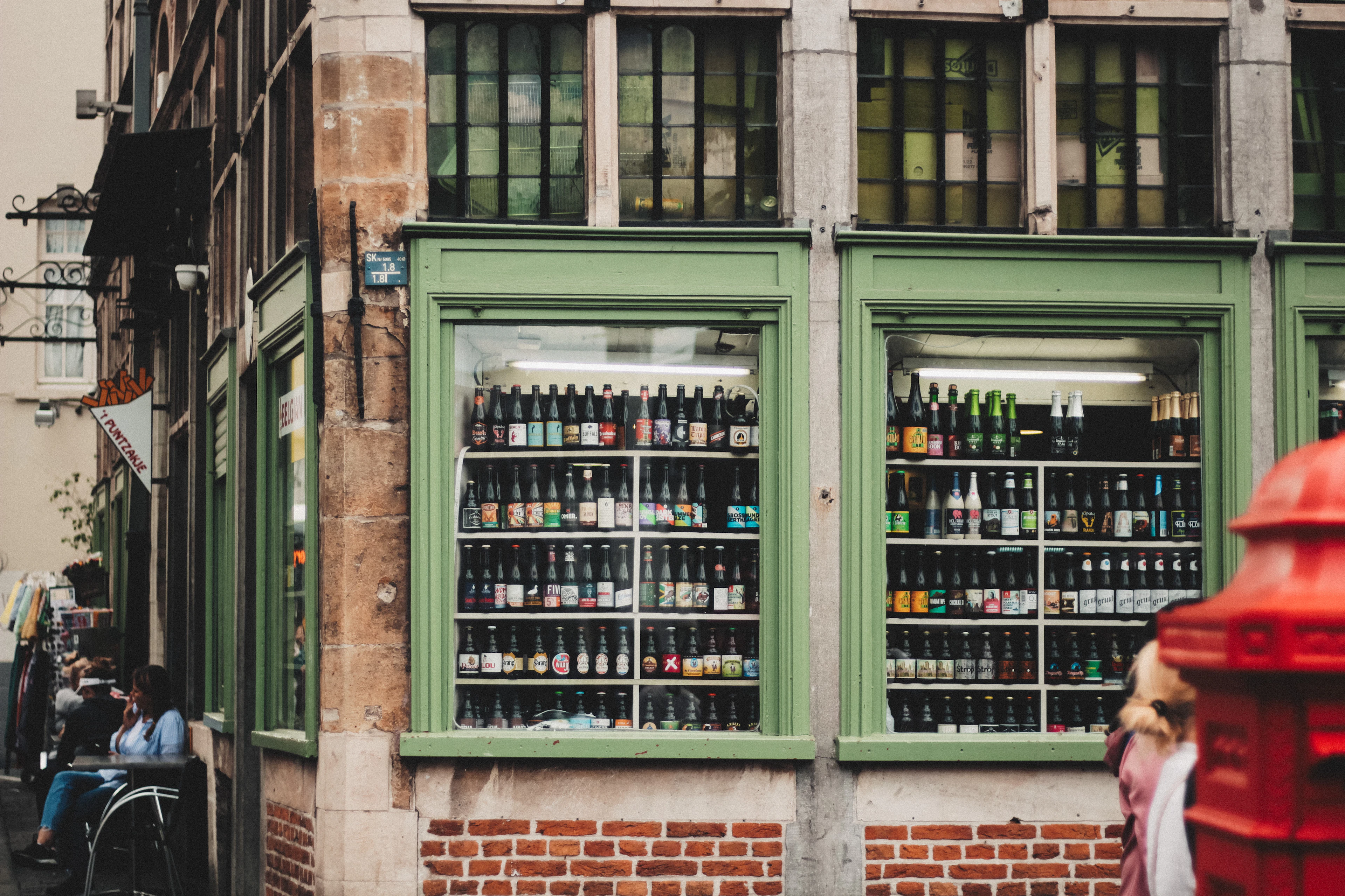 A green-framed Belgian shop window filled with rows of beer bottles on display.