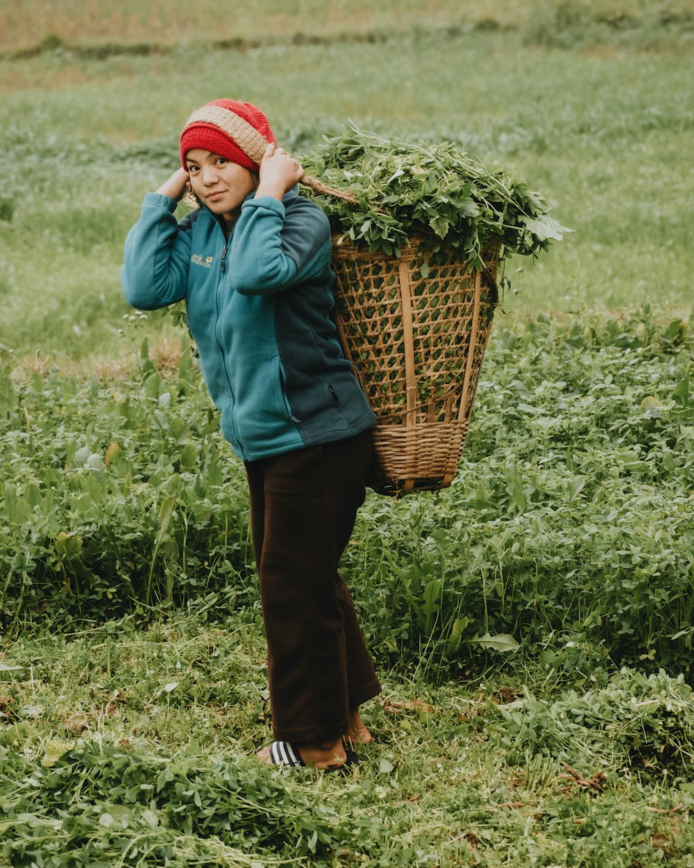 a woman standing in a field with a basket on her shoulder