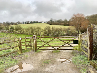 A sturdy wooden gate fitted at the entrance of a rural farm property.