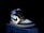 A stylish athletic shoe is placed on a shoebox, featuring a combination of black, white, and light blue. The shoe design includes a prominent logo on the side and a high-top silhouette.