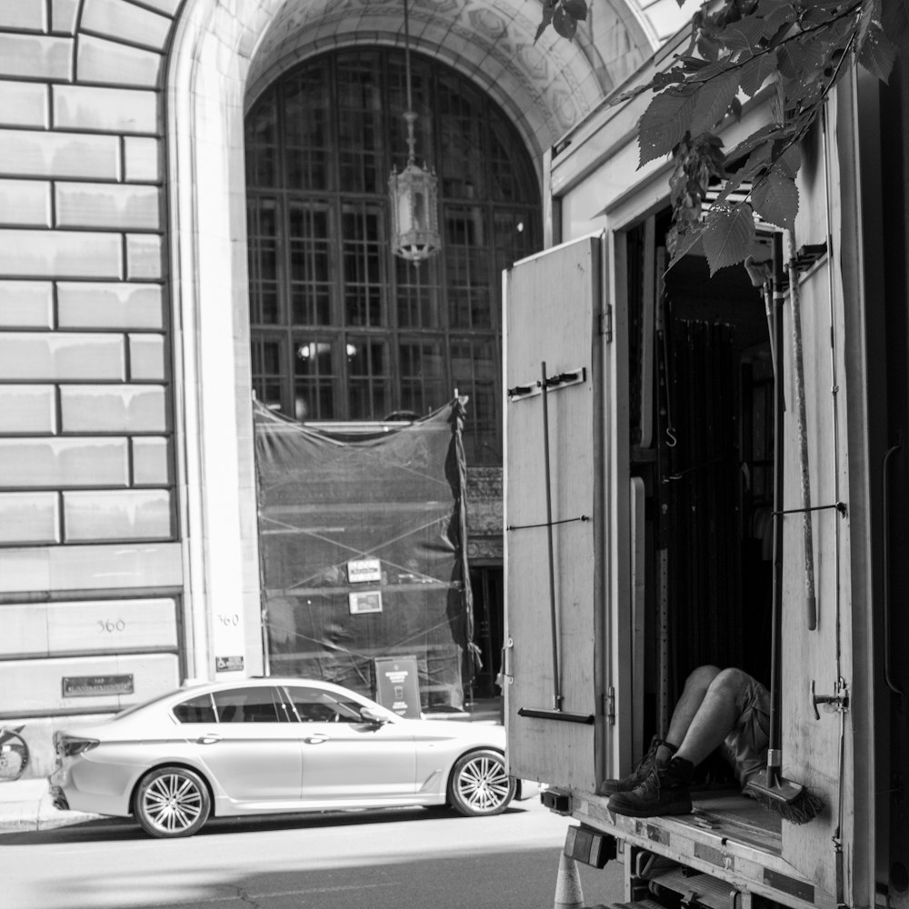 a man sitting in the doorway of a building next to a car