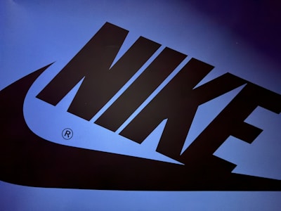 The image features a large, bold Nike logo in black set against a gradient blue background. The logo includes the word 'NIKE' and the iconic swoosh design.