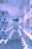 A brightly lit aisle lined with numerous vending machines on both sides, displaying various colorful items inside them. The machines have a modern, clean design, and the floor is carpeted. The ceiling has several spotlights and decorations with vibrant patterns are hanging overhead.