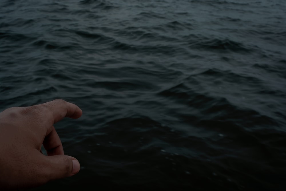 a person's hand pointing towards the water