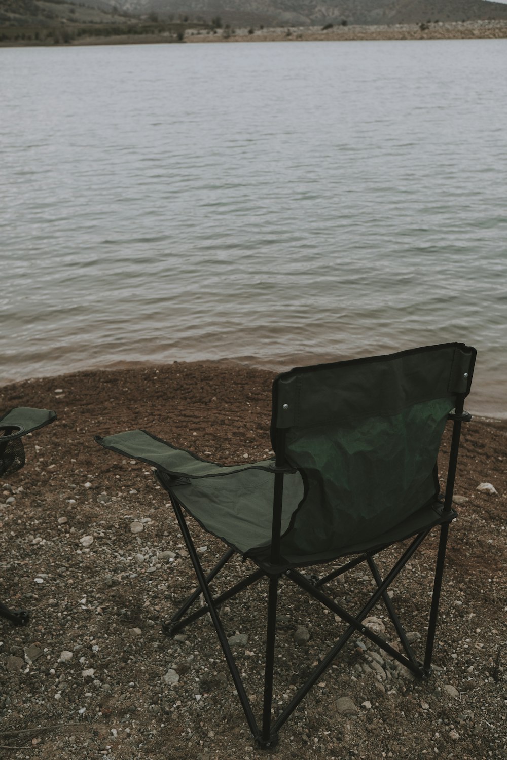 a green chair sitting on top of a beach next to a body of water