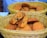 A wicker basket contains a pile of freshly baked cookies with chocolate chips. One cookie is broken in half, revealing a soft interior filled with dark chocolate bits. The cookies have a golden-brown color and appear slightly crispy on the edges.