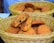 A wicker basket contains a pile of freshly baked cookies with chocolate chips. One cookie is broken in half, revealing a soft interior filled with dark chocolate bits. The cookies have a golden-brown color and appear slightly crispy on the edges.