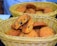 A wicker basket contains a pile of freshly baked cookies with chocolate chips. One cookie is broken in half, revealing a soft interior filled with dark chocolate bits. The cookies have a golden-brown color and appear slightly crispy on the edges.